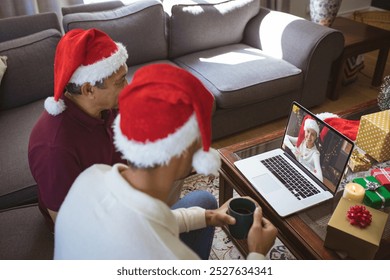 Biracial father and adult son in santa hats making laptop christmas video call with smiling woman. christmas, festivity and communication technology. - Powered by Shutterstock