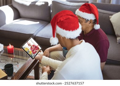 Biracial father and adult son in santa hats making tablet christmas video call with female friend. christmas, festivity and communication technology. - Powered by Shutterstock