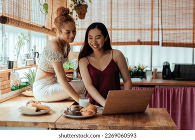 Biracial female couple spending morning at home in the kitchen and using technology - Powered by Shutterstock