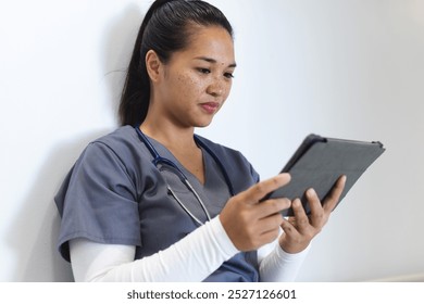 Biracial female doctor wearing scrubs using tablet in hospital corridor. Medicine, healthcare, communication, work and hospital, unaltered. - Powered by Shutterstock