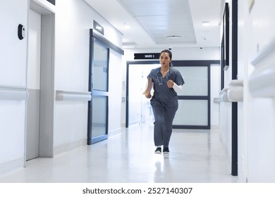 Biracial female doctor wearing scrubs running through corridor in hospital, copy space. Medicine, healthcare, work and hospital, unaltered. - Powered by Shutterstock