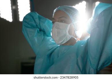 Biracial female surgeon wearing surgical gown and face mask in operating theatre at hospital. Hospital, surgery, hygiene, medicine, healthcare and work, unaltered. - Powered by Shutterstock