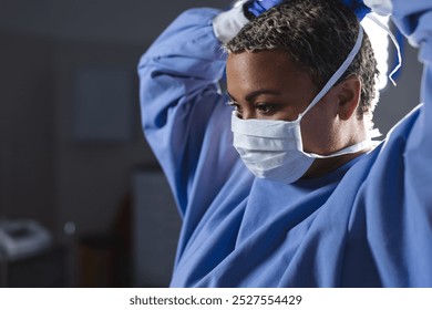 Biracial female surgeon wearing surgical gown and face mask in operating theatre. Medicine, healthcare, surgery, work and hospital, unaltered. - Powered by Shutterstock