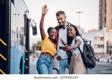 Biracial friends taking selfie with a smartphone while standing at a bus stop and waiting for public transport at sunny bright day. Multiracial passengers waiting for a bus. Diversity. - Powered by Shutterstock