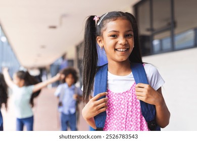 Biracial girl with backpack smiling at school. Other students playing near school building, creating lively atmosphere, unaltered - Powered by Shutterstock