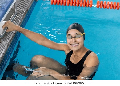 Biracial girl in goggles grips indoor pool edge. Sporting friendly smile, dark hair in a swim cap, and maintaining a fit physique, she exudes confidence and readiness, unaltered - Powered by Shutterstock