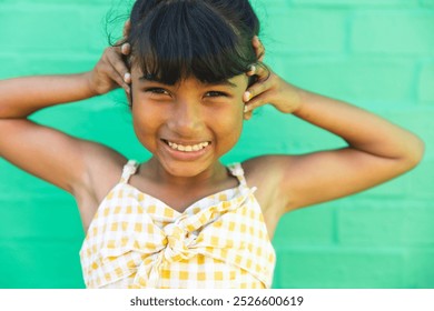 Biracial girl smiles brightly against a green background. Her cheerful expression adds a lively vibe to the outdoor setting. - Powered by Shutterstock