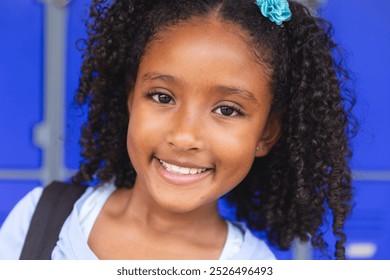 Biracial girl smiles brightly in front of a blue door at school. Her cheerful expression suggests excitement for a school day ahead. - Powered by Shutterstock