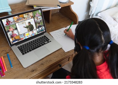 Biracial girl writing english notes in book while attending online class over video call on laptop. Home, unaltered, childhood, wireless technology, education, student and e-learning concept. - Powered by Shutterstock