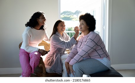 Biracial Happy Female Friends Applying Make-up On Young Woman's Face With Afro Hair At Home. Copy Space, Skin Care, Pampering, Beauty Product, Unaltered, Friendship, Togetherness, Lifestyle.