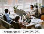 Biracial highly skilled programmer team writing codes surrounded by digital devices, coffee and snacks while sitting at white wooden table in roomy light modern office