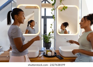 Biracial lesbian couple brushing teeth and talking in bathroom. Lifestyle, relationship, togetherness, self care, hygiene and domestic life, unaltered. - Powered by Shutterstock