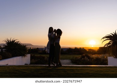 Biracial lesbian couple dancing in garden at sunset. Lifestyle, relationship, togetherness, nature and domestic life, unaltered. - Powered by Shutterstock