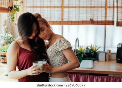 Biracial Lesbian couple in love, standing in the kitchen, hugging and drinking some milk - Powered by Shutterstock