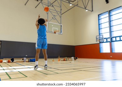 Biracial male basketball player wearing blue sports clothes and shooting basketball at gym. Sport, activity and lifestyle, unaltered, copy space. - Powered by Shutterstock