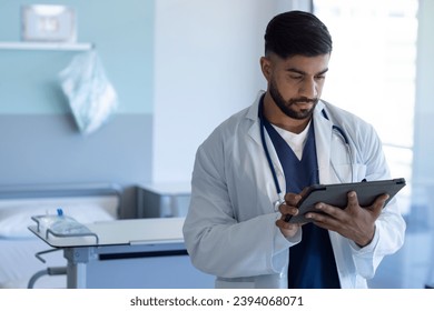 Biracial male doctor using tablet in sunny hospital room. Medicine, healthcare, communication and medical services, unaltered. - Powered by Shutterstock