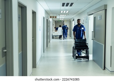 Biracial male healthcare worker pushing empty wheelchair in busy hospital corridor. Hospital, medical and healthcare services. - Powered by Shutterstock