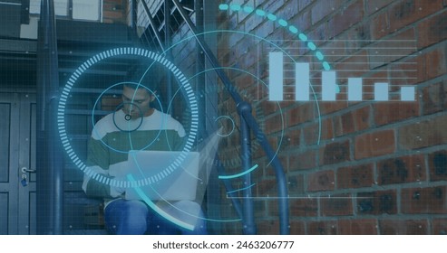 Biracial male sitting, using laptop, looking focused. He has short black hair, wearing casual clothes, against brick wall - Powered by Shutterstock