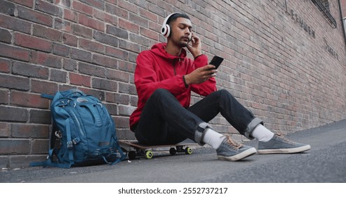 Biracial man sitting on skateboard and listening to music in the street. backpacking holiday city travel break. - Powered by Shutterstock