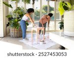 Biracial mother and adult daughter paint stool in casual clothes. Both with focused expressions, they share a creative moment at home, unaltered