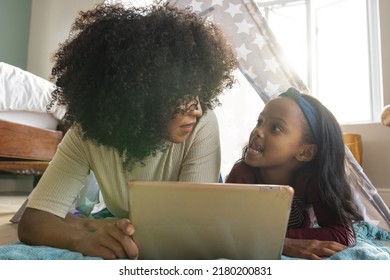 Biracial Mother With Afro Hair Talking With Daughter While Relaxing In Blanket Tent At Home. Wireless Technology, Camping, Unaltered, Family, Togetherness, Childhood, Lifestyle And Home.