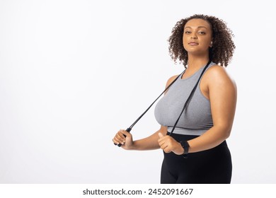 Biracial plus size model with resistance band on a white background, copy space. She has curly brown hair, light brown skin, and sports attire, promoting body positivity, unaltered - Powered by Shutterstock