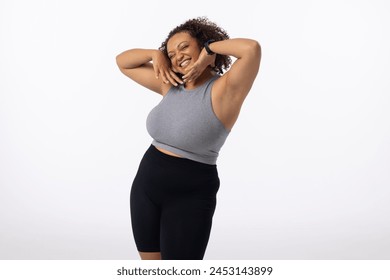 Biracial plus size young female model poses, hands on head, smiling, white background, copy space. With curly brown hair and brown eyes, she wears casual sportswear, promoting body positivity - Powered by Shutterstock