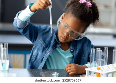 Biracial schoolgirl in safety glasses using pipette in science class with copy space. Education, inclusivity, childhood, elementary school and learning concept. - Powered by Shutterstock