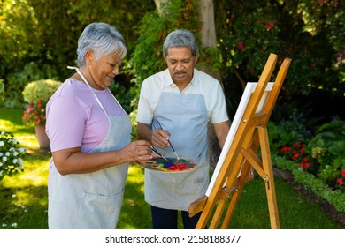 Biracial senior couple wearing aprons painting with watercolors on canvas against plants in yard. unaltered, nature, lifestyle, togetherness, love, painting, art, hobbies and retirement concept. - Powered by Shutterstock