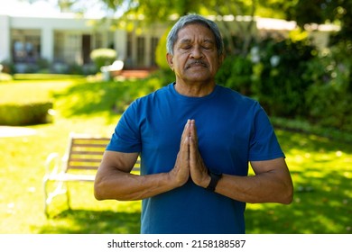 Biracial senior man with eyes closed meditating in prayer position against plants at yard. nature, zen, unaltered, retirement, yoga, fitness and active lifestyle concept. - Powered by Shutterstock