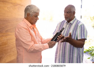 Biracial senior man receiving male friend with champagne bottle while standing in nursing home. Guest, alcohol, entrance, greeting, unaltered, togetherness, support, assisted living, retirement. - Powered by Shutterstock