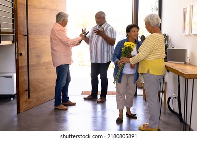 Biracial seniors receiving friends with bouquet and champagne bottle in nursing home, copy space. Entrance, guest, greeting, unaltered, togetherness, support, assisted living and retirement concept. - Powered by Shutterstock