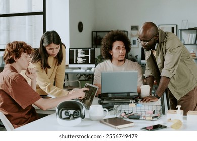 Biracial team of developers discussing codes on laptop during workday in office