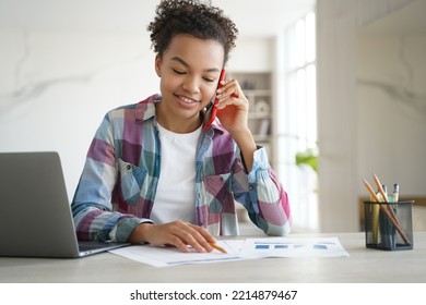 Biracial Teen Girl School Student Call By Phone, Discussing Homework With Friend, Sitting At Desk With Laptop. Smiling Biracial Schoolgirl Chatting With Classmate By Mobile While Learning At Home.