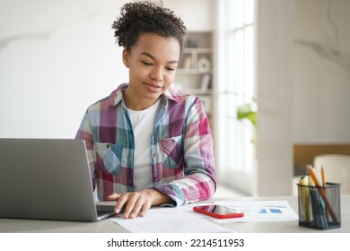 Biracial Teen Girl Student Learning At Laptop Look On Mobile Phone, Reading Message In Social Networks. Modern Biracial Schoolgirl Distracted From Study, Homework. Gadget Addiction Concept.