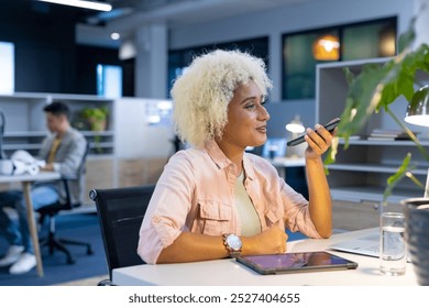 Biracial woman using smartphone in modern office for business. Open-plan workspace with colleagues working in background, unaltered - Powered by Shutterstock