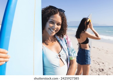 Biracial women enjoy a sunny beach day. They hold surfboards, ready for an exciting day of surfing in the outdoor setting. - Powered by Shutterstock