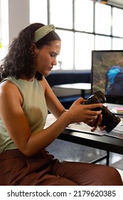 Biracial Young Businesswoman Examining Camera At Desk In Creative Office. Unaltered, Creative Business, Workplace, Photography Themes.