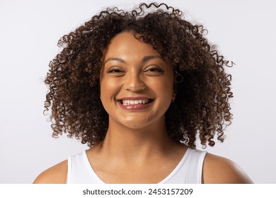 A biracial young plus size model smiles, wearing white tank top. She has curly brown hair and light brown skin on a white background, promoting body positivity with minimal makeup - Powered by Shutterstock