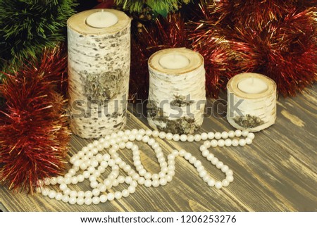 Birch candlesticks and beads made of artificial pearls, red and green knick-knackery. Gray wooden background.