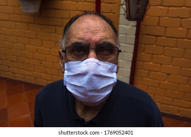 Bird Eye Angle Photography Of An Old Man (+70) With A White Face Mask, Glasses And A Blue Sweater Stand Up In The Backyard Looking At Camera. Profile Portrait