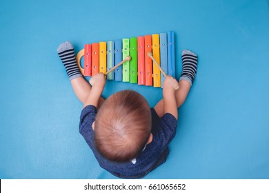 Bird eye view of Cute little Asian 18 months / 1 year old baby boy child hold sticks & plays a musical instrument colorful wooden toy xylophone, Educational toy for kids and toddlers concept 