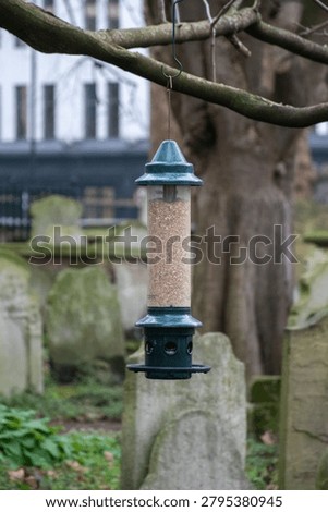 A bird feeder designed to keep squirrels away, set against a serene graveyard backdrop.