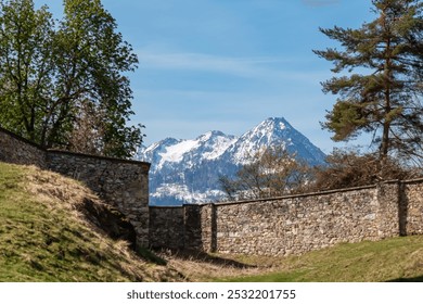 Bird flying over historical stone wall with panoramic view of snow-capped mountain peak Mittagskogel seen from zoo Tierpark Rosegg, Carinthia, Austria. Tranquil scene in Rosental Valley, Austrian Alps - Powered by Shutterstock