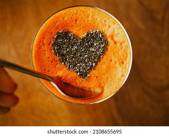 bird view of a glass on wooden table with healthy cold pressed carrot orange juice and chiaseeds on top in the form of heart to symbolize the love passion for a detox juice fast  with dipping spoon
