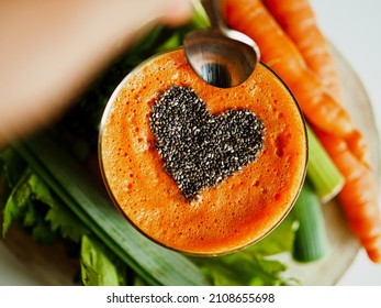 bird view of a glass on wooden table with healthy cold pressed carrot orange juice and chiaseeds on top in the form of heart to symbolize the love passion for a detox juice fast  with dipping spoon