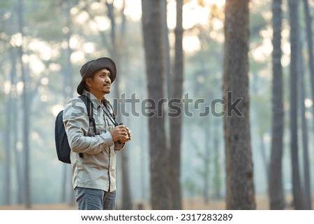 Bird watcher is looking through binoculars while exploring in the pine forest for surveying and discovering the rare biological diversity and ecologist on the field study