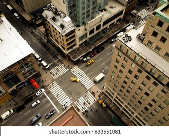 Birds Eye View Of 5th Avenue, A Yellow Taxi Makes A Left Hand Turn. Looking Down On Midtown Manhattan's Fifth Avenue, Zebra Crossing And People Going To Work. Top View Of New York City Street.