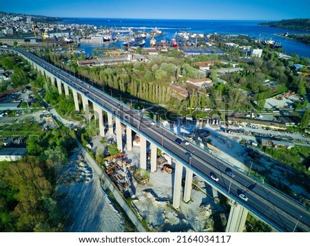Bird's eye view of concrete sturdy road bridge between land of modern infrastructure seaside city of Sozopol with multi-storey architectural resort houses, near deep blue rippled Black Sea
