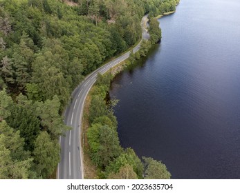 Bird's eye view of a curvy road next to water.  Aerial, drone photography taken from above in Sweden in summer. Surroundings with trees and a lake. Copy space and place for text. Travel concept.